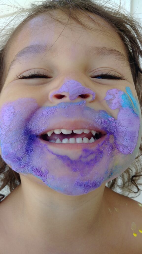 a little girl with purple paint all over her face. honest truths of being stay-at-home mom, life is messy 