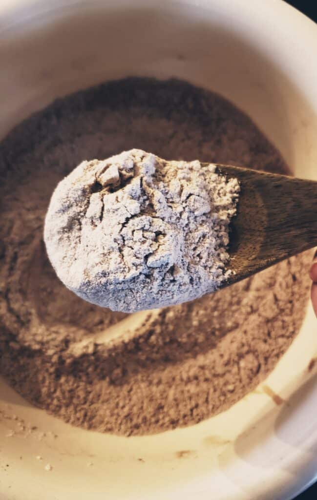 flour, cocoa powder, salt, and cinnamon combined in a mixing bowl with a wooden spoon 