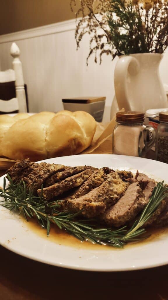 a roasted tenderloin on a plate of rosemary, rolls, and a made winter table. winter homemaking 